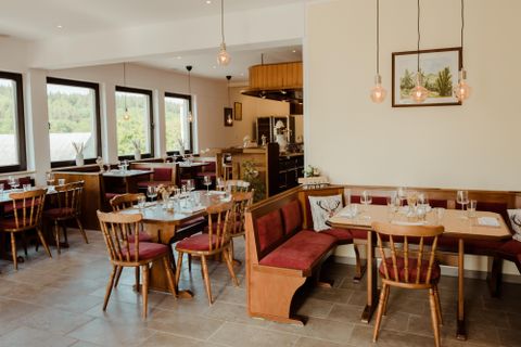 Ein modernes Restaurant mit Holzstühlen und Tischen. Die große Fensterfront sorgt für viel natürliches Licht.