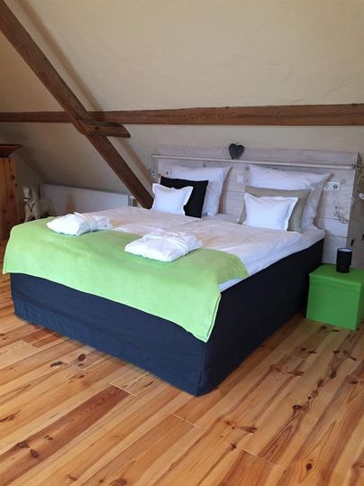 A cozy bedroom with a large bed and fresh white bedspreads. The walls are made of wood, and a green throw adds color to the room.