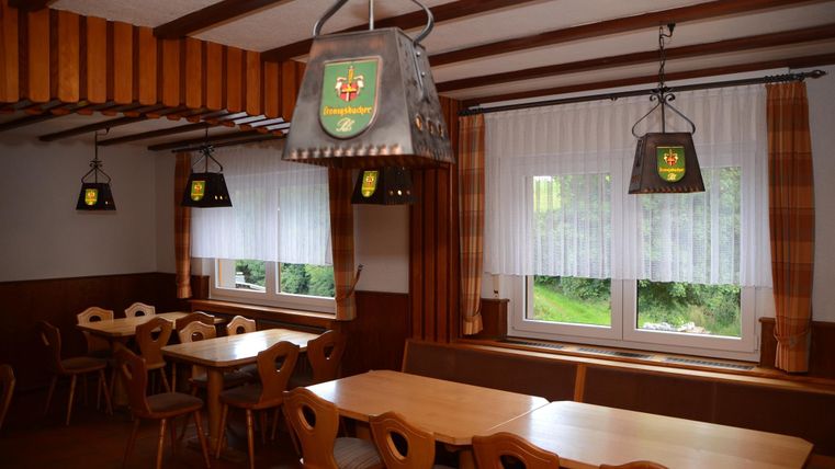 Ein gemütlicher Raum mit Holzdekor und mehreren Tischen. Die Fenster sind mit Vorhängen bedeckt und leuchten in das Innere.