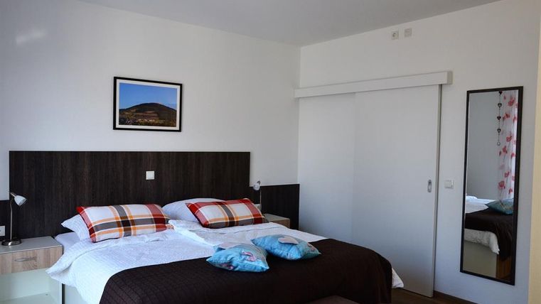 A modern bedroom with two beds and colorful cushions. A picture and a mirror hang on the wall, and the room appears bright and friendly.
