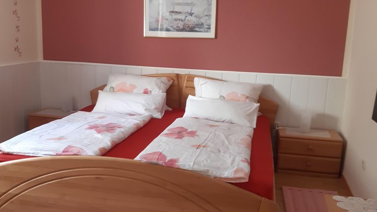 Ein helles Schlafzimmer mit einem Doppelbett und zwei einzelnen Betten. Die Wände sind rot und mit einem Bild dekoriert, und ein Teppich liegt am Boden.