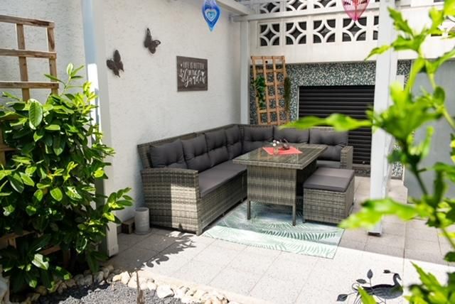 Ein gemütlicher Außenbereich mit einer Sofagruppe aus Rattan und einem Tisch. Umgeben von Pflanzen und dekorativen Elementen, bietet der Raum eine einladende Atmosphäre.
