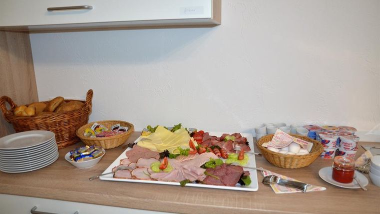 A buffet with various types of sausages and cheeses on a white plate. Next to it lies fresh bread and various spreads in baskets.