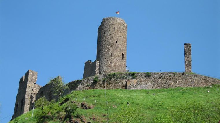 An old castle on a hill, surrounded by green meadow. The sky is clear and blue.