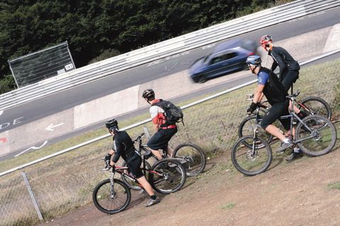 Vier Mountainbiker beobachten ein Auto auf einer Rennstrecke.