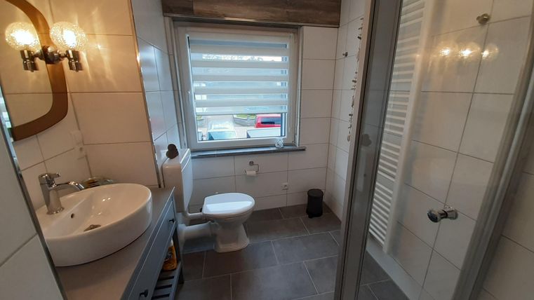 Ein modernes Badezimmer mit einem Waschbecken, einer Toilette und einer Dusche. Die Wände sind hell gefliest, und ein Fenster sorgt für Tageslicht.
