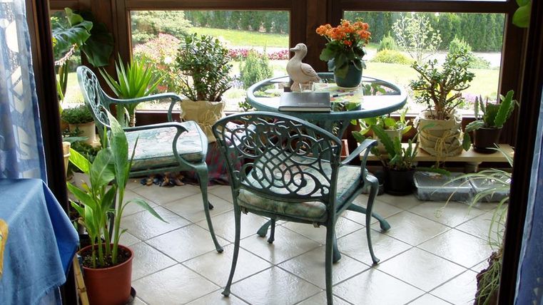 A cozy conservatory with a round table and two chairs. Surrounded by plants and a beautiful view outdoors.