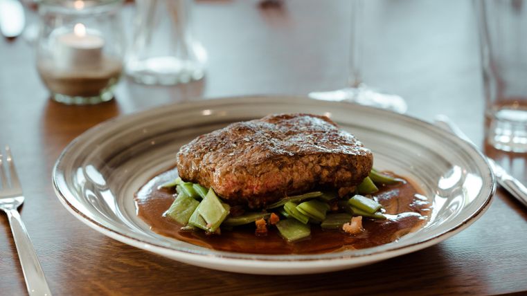 Ein saftiges Stück Fleisch auf einem Bett aus Gemüse, serviert in einer eleganten Schüssel. Der Teller ist ansprechend angerichtet und vermittelt eine erlesene Atmosphäre.
