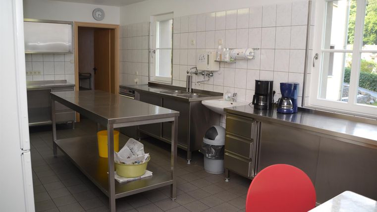 Eine moderne Küche mit Edelstahlmöbeln und einem großen Arbeitstisch. Sie ist hell und gut ausgestattet mit verschiedenen Küchengeräten.