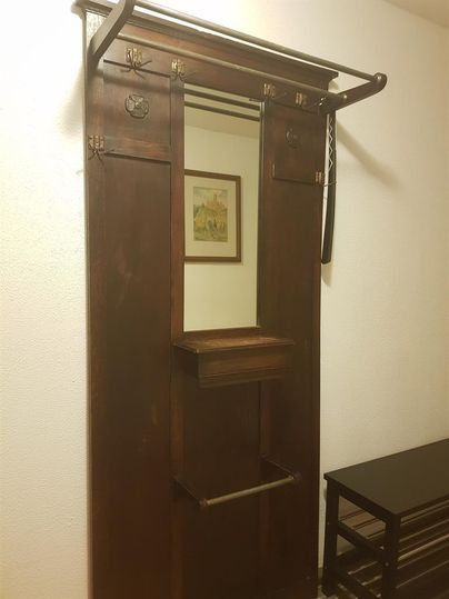 A wooden wardrobe with a top rod for hanging and a small shelf. In the background, a framed picture is visible.