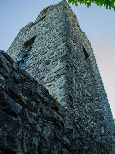 Ein steinerner Turm ragt in den Himmel, umgeben von Bäumen. Die Struktur zeigt alte Architektur und historische Merkmale.