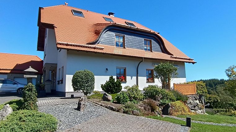 Ein charmantes Haus mit rotem Dach und schönem Garten. Die klare blaue Himmel verleihen der Umgebung eine einladende Atmosphäre.