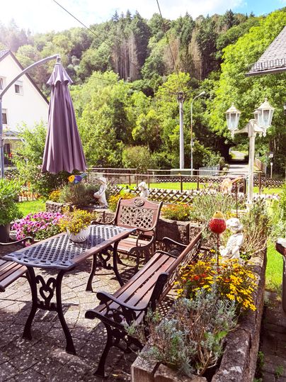 Ein einladender Gartenbereich mit einem Tisch und Stühlen aus Metall. Umgeben von bunten Blumen und grünen Bäumen ist es ein schöner Ort zum Entspannen.