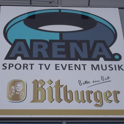 Ein Schild mit der Aufschrift "ARENA" und den Worten "SPORT TV EVENT MUSIK". Darunter steht "Bitburger" in goldenen Buchstaben.