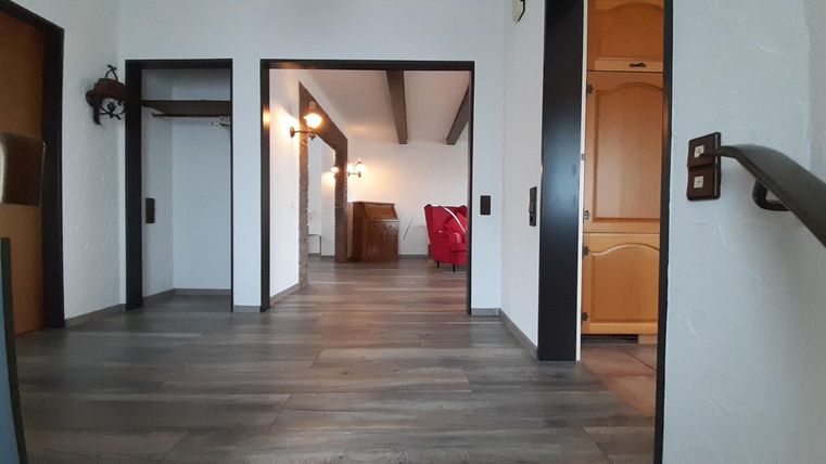 Ein heller Flur mit Holzfußboden und weißen Wänden. Im Hintergrund sind Möbel und mehr Räume sichtbar.