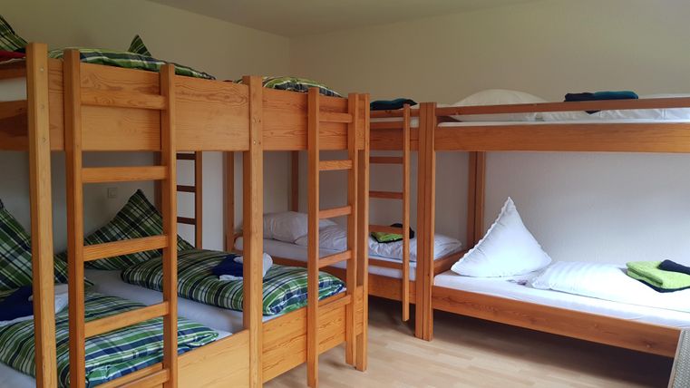 Ein Gemeinschaftsraum mit mehreren Etagenbetten aus Holz. Die Betten sind mit bunten Kissen und Decken ausgestattet.