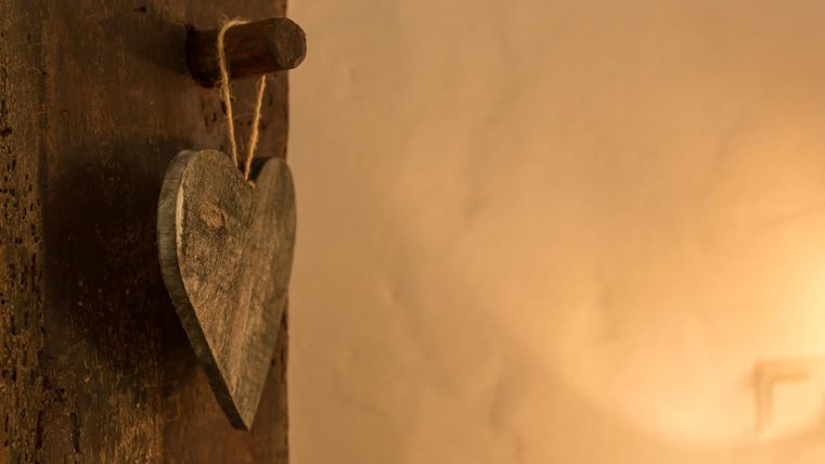 A wooden heart hangs from a door handle. The background is softly lit and conveys a cozy atmosphere.