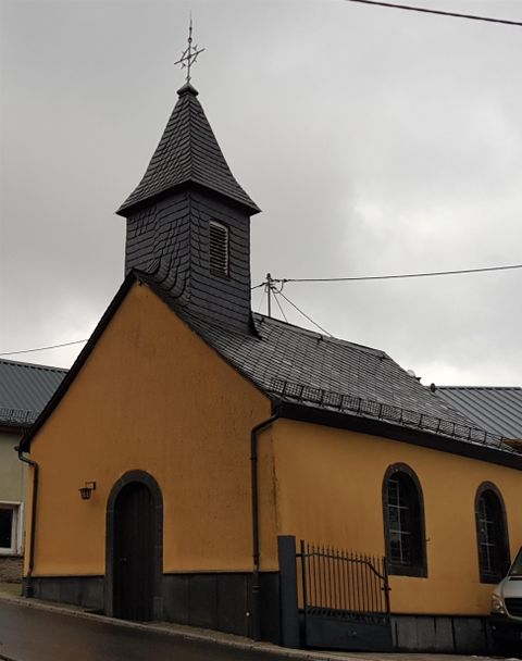 A small, yellow church with a pointed roof and a tall tower. The sky is cloudy and the surroundings seem tranquil.
