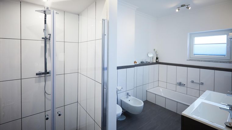 A modern bathroom with a shower cabin on the left side and a bathtub on the right side. The walls are brightly tiled and the room design is simple and elegant.