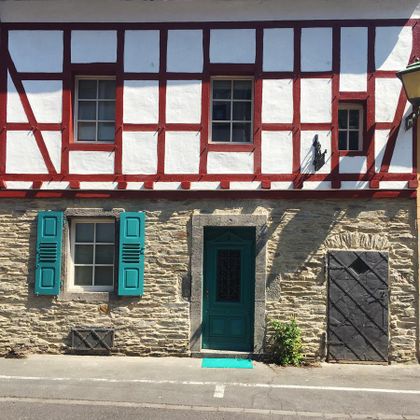Ein charmantes Fachwerkhaus mit weißem Putz und roten Balken. Die Tür ist grün und es gibt grüne Fensterläden.