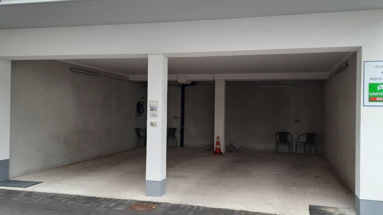 An empty garage with white walls and a gray floor. There are some chairs present and a sign on the wall.