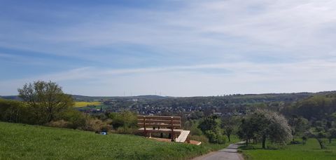 Eine malerische Landschaft mit sanften Hügeln und blauen Himmel. Im Vordergrund steht ein Holzgebäude, umgeben von Wiesen und Bäumen.
