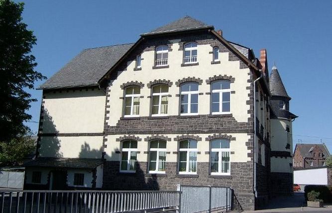 Ein historisches Gebäude mit einer Mischung aus Stein und Putz. Es hat viele Fenster und einen turmförmigen Anbau.