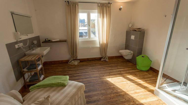 A simple and bright room with wooden floors and large windows. There is a shower, a sink, and a cozy sitting area.