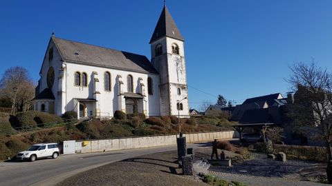 Eine schöne Kirche mit einem hohen Turm steht an einer ruhigen Straße. Der Himmel ist klar und blau.