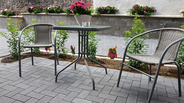 A cozy outdoor area with a table and two chairs. Blooming plants adorn the surroundings and create an inviting atmosphere.