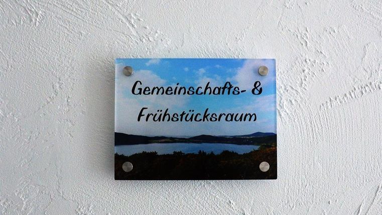 A sign reading "Community & Breakfast Room" hangs on a wall. In the background, a picturesque landscape with water and hills can be seen.