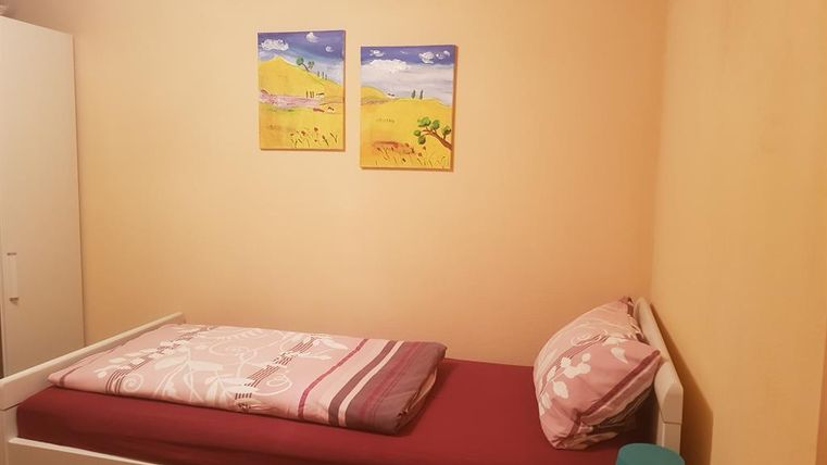 A simple bedroom with a bed and a small nightstand. Two colorful pictures hang on the wall.