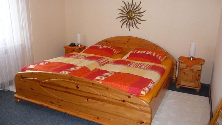 A cozy bedroom with a large wooden bed and colorful bedspreads. There are two nightstands and a decorative wall object.