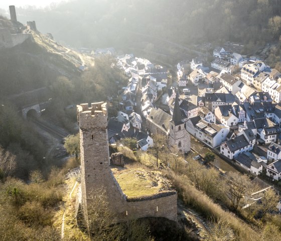 Luftaufnahme von Monreal mit einer Burg im Vordergrund und Fachwerkh&auml;usern im Tal. Die Landschaft ist von B&auml;umen und H&uuml;geln umgeben., &copy; Eifel Tourismus GmbH, D. Ketz