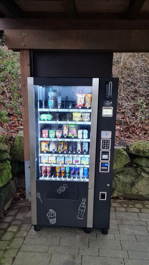 A vending machine is located under an overhang. It offers a selection of snacks and drinks.