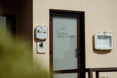An entrance to a country house called "Eifelstube". The door has a clear label and is surrounded by a bright wall.