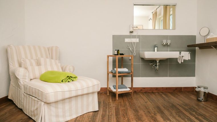 A cozy room with a comfortable armchair and a modern sink. The floor is made of wood, and there are some decorative elements.