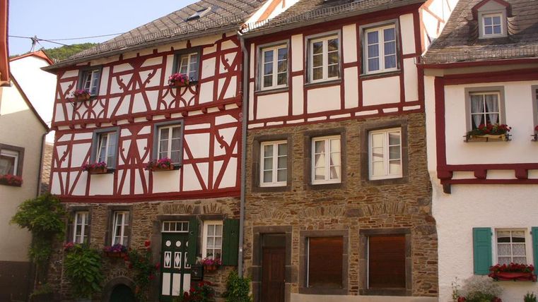 Ein charmantes Fachwerkhaus mit bunten Blumen und grünen Pflanzen. Daneben steht ein traditionelles Steinhaus mit Holzfenstern.