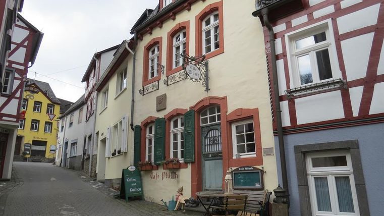 Eine charmante Straße mit traditionellen Häusern. Im Vordergrund steht ein Gasthaus mit grün-rot gestrichenen Fenstern.