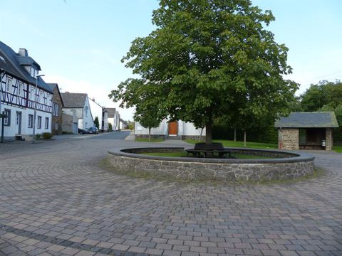 A quiet place with a large tree in the center. Surrounding the square are traditional houses and a stone bench.