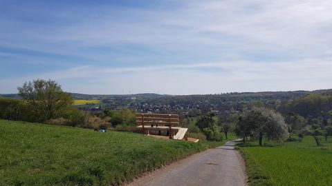 A picturesque landscape with gentle hills and a clear sky. In the foreground is a road leading to a small building.