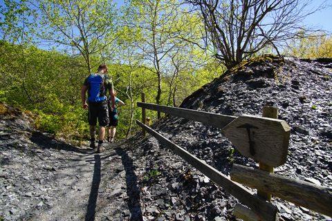 Zwei Wanderer auf einem schmalen Pfad in einer Schieferlandschaft, umgeben von grünen Bäumen und blauem Himmel.
