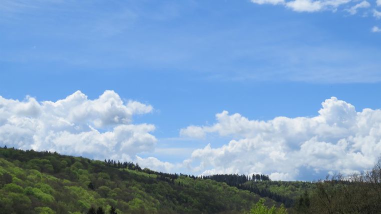Eine malerische Landschaft mit grünen Hügeln und einem klaren blauen Himmel. Dicke, weiße Wolken ziehen sanft vorbei.