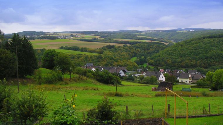 A hilly landscape with green meadows and small villages. The sky is cloudy and the surroundings appear peaceful and rural.