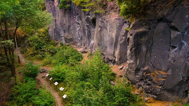 A natural area with high rocks and lush greenery. A narrow path leads through the landscape.
