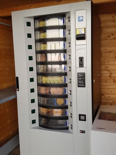 A snack vending machine with various compartments. The machine is located in a wooden room.