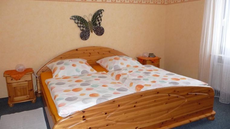 A cozy bedroom with a large double bed and colorful bed covers. The walls are light yellow and adorned with a butterfly decoration.