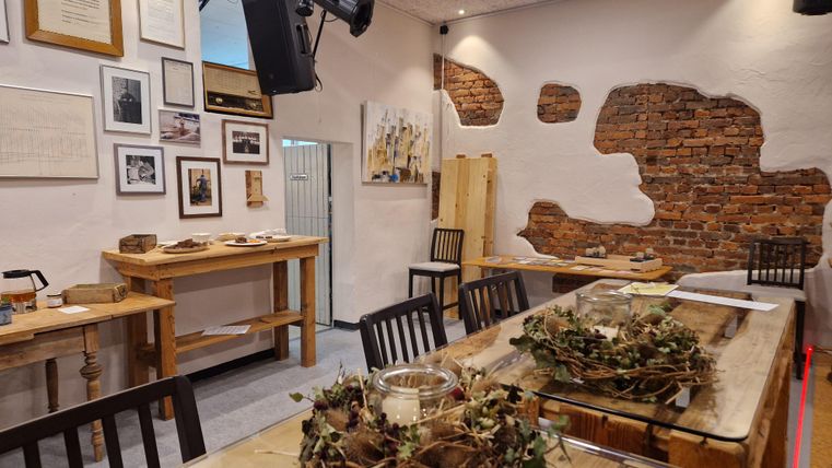 A cozy room with wooden furniture and a brick wall.
Pictures hang on the walls, and on the table are decorations made of plants.