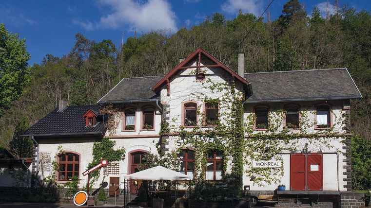Ein charmantes Gebäude mit einer Fassade, die von Pflanzen umschlungen ist. Im Vordergrund steht eine Terrasse mit Tischen und Stühlen.