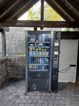 A vending machine is located under a roof. It offers a selection of snacks and drinks.